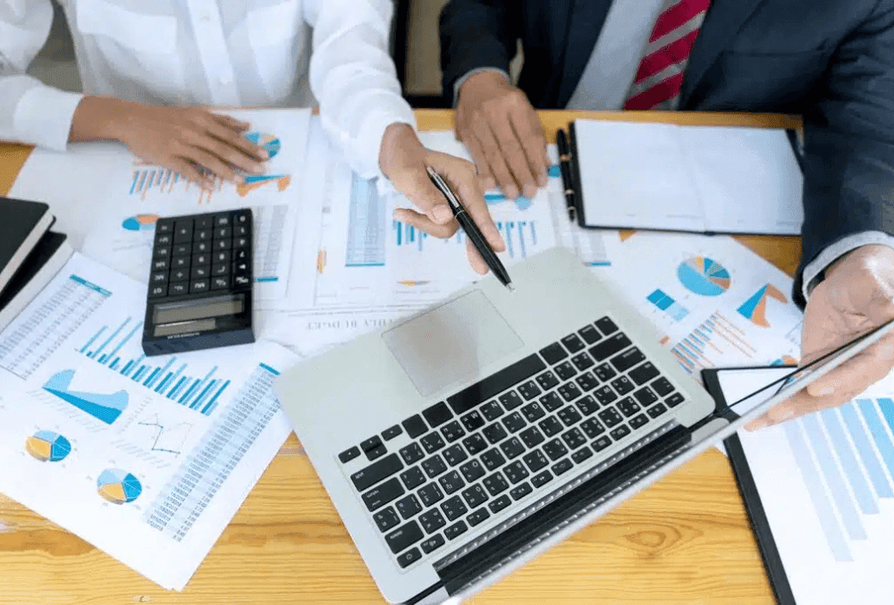 A financial consultant analyzes franchise financial reports on a laptop, surrounded by charts, graphs, and a calculator. In the background, a busy franchise storefront represents business success and profitability.